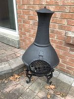 Full front view of black metal chiminea on brick patio