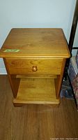 Front view of one pine wood end table showing drawer with wooden knob and lower shelf.