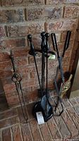 Photo of fireplace tool set on stand and additional fireplace tools against brick background, showing condition and tool details.