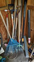 Photo of assortment of garden tools including rakes, forks, shovels, and mesh roll stored inside a wooden shed