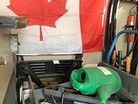 Wooden wagon loaded with green watering can, various gardening tools, hose parts, and white pails in the background, with a Canadian flag hung behind