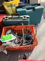 Overview of multiple power tools and cases in an orange basket and behind it, along with some hardware packages and accessories scattered around.