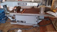 Full side view of Delta 15-inch scroll saw showing entire machine and attached power cord, surface rust on table and base.