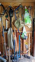 Tools including sledgehammers, clamps, saw, gloves, and cables hanging on shed wall