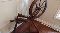 Side angle view of vintage wooden spinning wheel showing wheel, legs, and spindle mechanism.