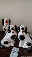 Front view of two black and white Staffordshire spaniel dog figurines and one orange snout dog figurine, all ceramic, on surface with auction tag.