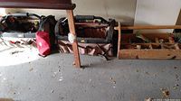Four tool bags/tool belts hanging under a shelf with assorted tools visible inside and around them.