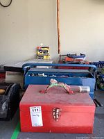 Two metal toolboxes stacked, showing the red toolbox on top with visible handle and latch, older condition with dust.