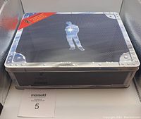 Metal tin box with Alex Rider silhouette and rivet design on lid, some wear and dents visible.