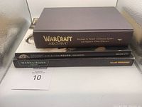 Stack of three gaming books viewed from the spine side: Warcraft Archive hardcover without slip cover, NieR Automata Art Book in black hardcover with Japanese text, and Warhammer 40,000 softcover rulebook.