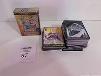 Photo showing sealed Naruto trading card tin and a large stack of Weiss Schwarz trading cards.