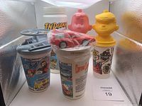 Front view showing five vintage collector cups with character toppers and printed graphics.