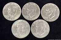 Obverse side of five Eisenhower Dollars showing profile of Eisenhower with dates 1971, 1972, and 1976 (two Bicentennial coins dated 1776-1976). Coins are in protective sleeves.
