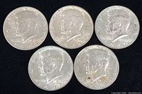 Obverse side of 5 Kennedy Half Dollar coins dated 1964 (two coins), 1967 (two coins), and 1968-D (one coin).