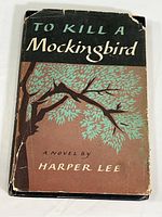 Front cover of the book showing the dust jacket with a tree branch illustration and title 'To Kill A Mockingbird' by Harper Lee. Dust jacket shows wear and tear on edges and corners.