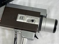 Close-up photo of the Canon Zoom 318 Super 8 camera body showing the textured brown and silver design, zoom lens, and wrist strap.