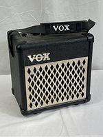 Front angle view of VOX mini guitar amplifier with protective metal grill and VOX branded shoulder strap.