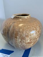 Front angle view of a rounded glazed pottery vase with a beige crystalline pattern and original artist tag attached at the neck.