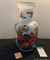 Full view of the decorative vase showing colorful floral and bird patterns on white ceramic with a gold rim.