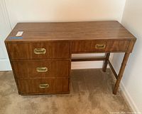 Photo of the wooden desk from front showing three drawers stacked on the left with recessed brass handles and turned wooden legs on the right.