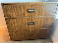 Front view of three-drawer wooden dresser showing wood grain and metal label pull handles.