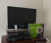 Photo showing RCA HDTV television, Sony Blu-ray player, Samsung DVD player, Insignia digital picture frame in box arranged on wooden surface, with power cords visible.