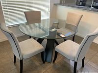Full view of the dining table and four upholstered chairs around it, showing glass top and chair design.