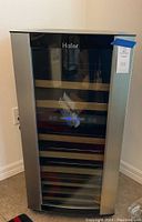 Front view of Haier wine cellar cooler, showing glass door with control panel and multiple wooden shelves inside.