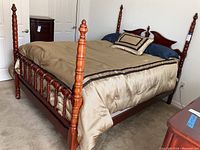 Queen size wooden poster bed with a satin brown/beige comforter, headboard and posts visible.