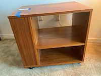 Front view of wooden rolling media console with adjustable shelf and caster wheels.