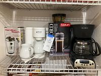 Photo shows four coffee-related items on a white wire shelf: Mr. Coffee drip coffee maker, Black & Decker small coffee maker with mug, Bodum Chambord French press box, and Hamilton Beach Custom Grind coffee grinder box.