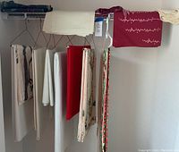 White, cream, and red table linens hanging on drying rack, viewed folded and draped for size and texture display