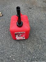 Photo of a red 2-gallon gas canister with black spout placed on pavement.
