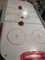 View of Haley Power Glide air hockey table showing the playing surface, three red pushers, puck, and side scoring system.
