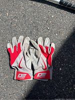 Pair of baseball batting gloves, red and white with Nike logos, shown palm side down on asphalt surface.