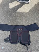 Image shows black padded protective gear with red stitching and adjustable straps designed for waist and leg fastening.
