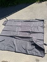 Photo of black car seat cover spread out on the ground showing front side and straps