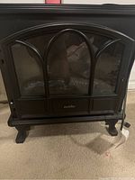 Front view of the black Duraflame electric fireplace showing the arched glass door and missing handle.