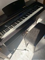 Full angled view of piano console, bench and power cable on carpeted floor