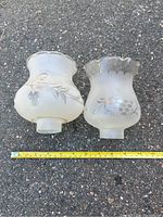 Two frosted glass lamp shades with floral and grapevine designs, showing differences in shape and rim style.