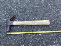 Single claw hammer placed on asphalt with measuring tape beside for scale showing approximately 13 inches in length.