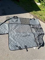 Full view of gray padded car seat cover for pets laid out flat on pavement, showing quilted pattern and attachment straps.