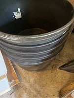 Stack of five large black plastic round planters shown from the side and above, showing ribbed sides and drainage holes in base.