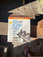 Box of electric roof deicing cable with label and instructions visible in outdoor daylight.