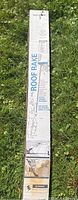 Photo of roof rake in its sealed original box placed on grass, showing brand and usage illustration on box.
