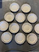 Twelve white salad plates arranged on the floor with visible decorative pierced lattice edges around each plate.