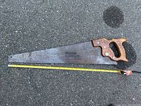 Photo showing the full hand saw including wooden handle and metal blade with a measuring tape laid beside it for scale.