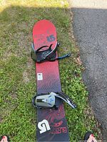 Top and side view of Burton snowboard showing the red and black gradient, binding details, and Burton logo.