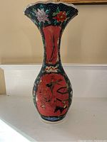 Front view of tall ceramic vase showing flared scalloped rim and painted Asian-style decorations including floral and figurative elements on red panels over dark background.