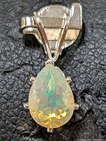 Close-up of pear-shaped opal pendant set in 10K gold on black textured background.